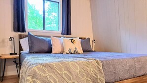 A bedroom with a wooden bed frame, a patterned bedspread, and a window with curtains. - Timber Point - Renovated Cabin on Indian Point (Branson)