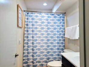A bathroom with a shower curtain featuring a fish pattern, a white sink, and a framed picture on the wall.