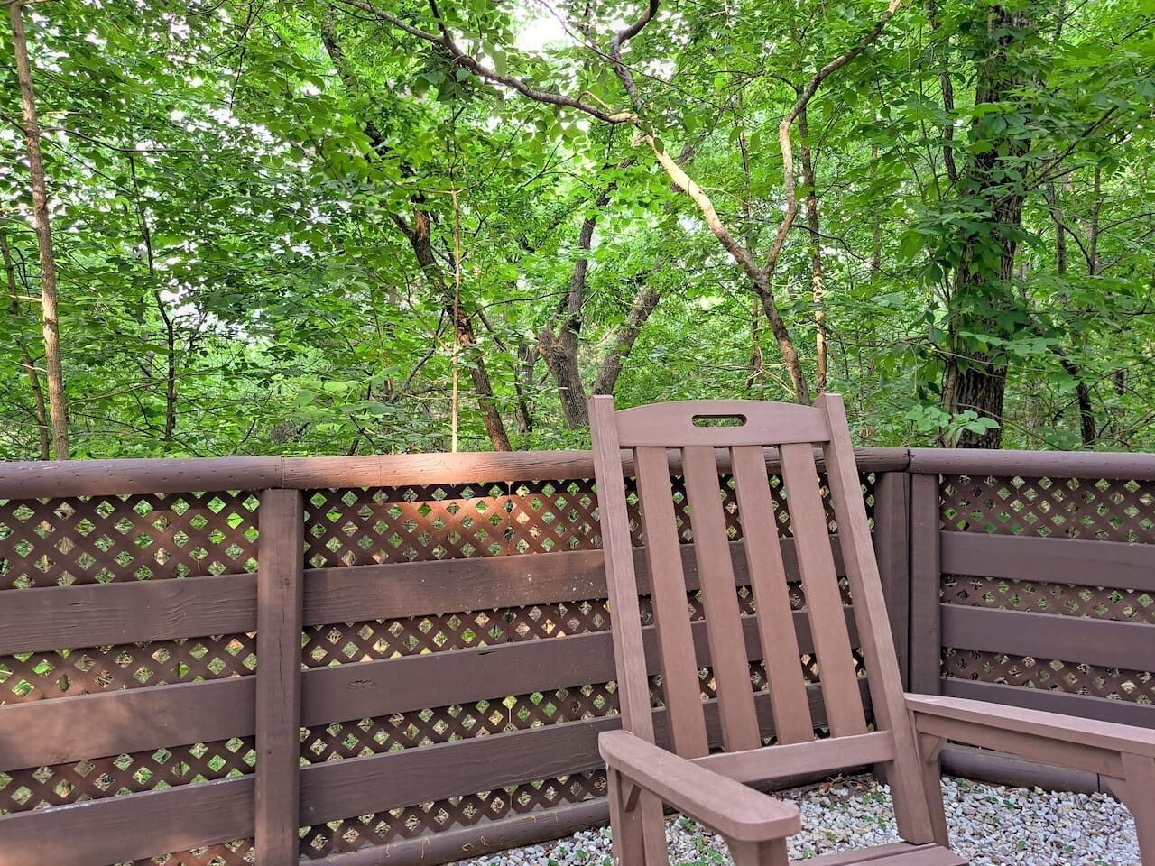 A wooden bench with a lattice backrest, situated in a wooded area.