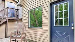 Una casa amb una porta blava, una cadira d'oscill·lar a l'exterior i una finestra amb vista a arbres.
