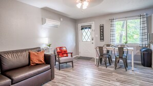 Ein Wohnzimmer mit braunem Ledersofa, einem kleinen Tisch mit Stühlen, einem Deckenventilator und einem Fenster mit Vorhängen.