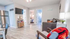 Ein modernes Wohnzimmer mit Sofa, eine Essecke mit Tisch und Stühlen, eine Küche mit Kühlschrank und ein Flur, der zum Schlafzimmer führt.