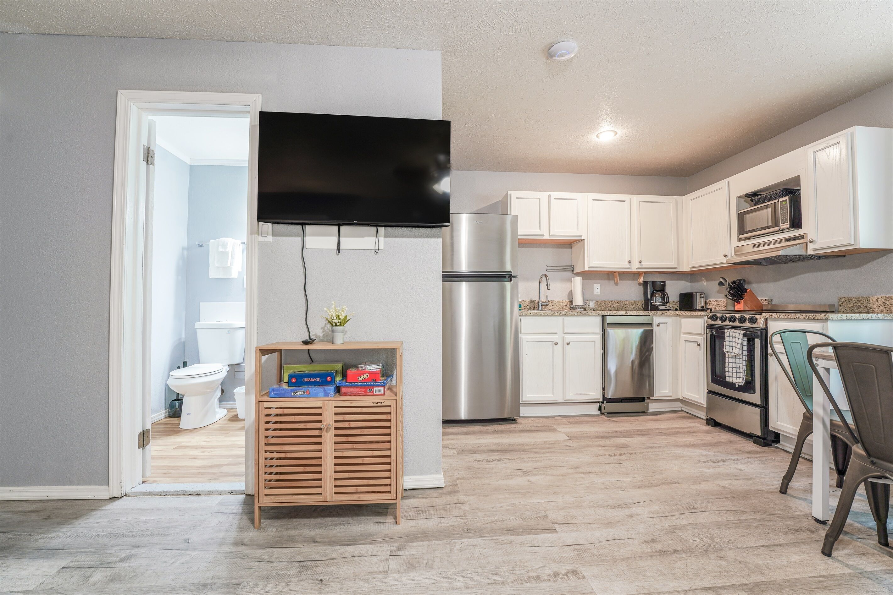 A modern kitchen with white cabinets, stainless steel appliances, and a flat-screen TV mounted above the refrigerator.