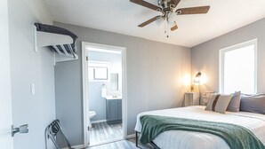 Een slaapkamer met een bed, een plafondventilator, een raam en een deur naar een badkamer.