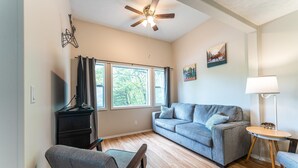 A living room with a grey sofa, wooden floor, ceiling fan, and a TV stand. - Tribesman Resort #2 - Renovated Cabin, Minutes to Silver Dollar, Great Location! (Branson)