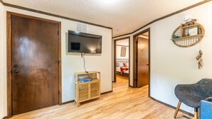 A hallway with a wooden door, a mounted TV, a wooden cabinet, and a blue chair. - Tribesman Resort #3 - Renovated Cabin, Minutes to Silver Dollar, Great Location! (Branson)