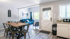A modern kitchen with a wooden table and chairs, a blue sofa, and a white door with a window. - Tribesman Resort #5 - Renovated Cabin, Minutes to Silver Dollar, Great Location! (Branson)