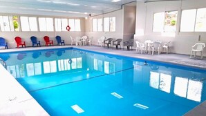En indendørs swimmingpool med krystalklart, blåt vand, omgivet af hvide og røde stole og borde.