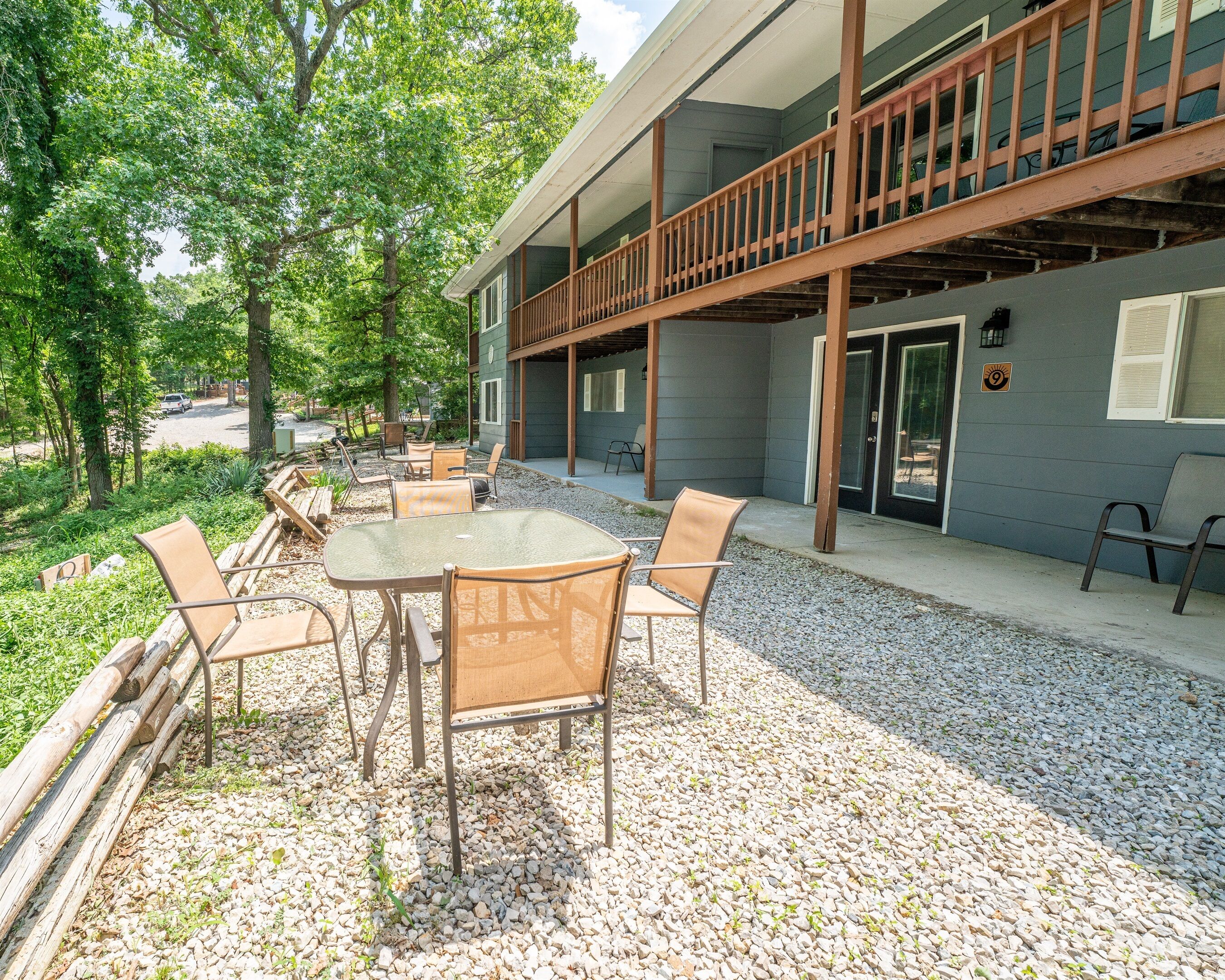 An outdoor patio with a table and chairs, surrounded by gravel and greenery.