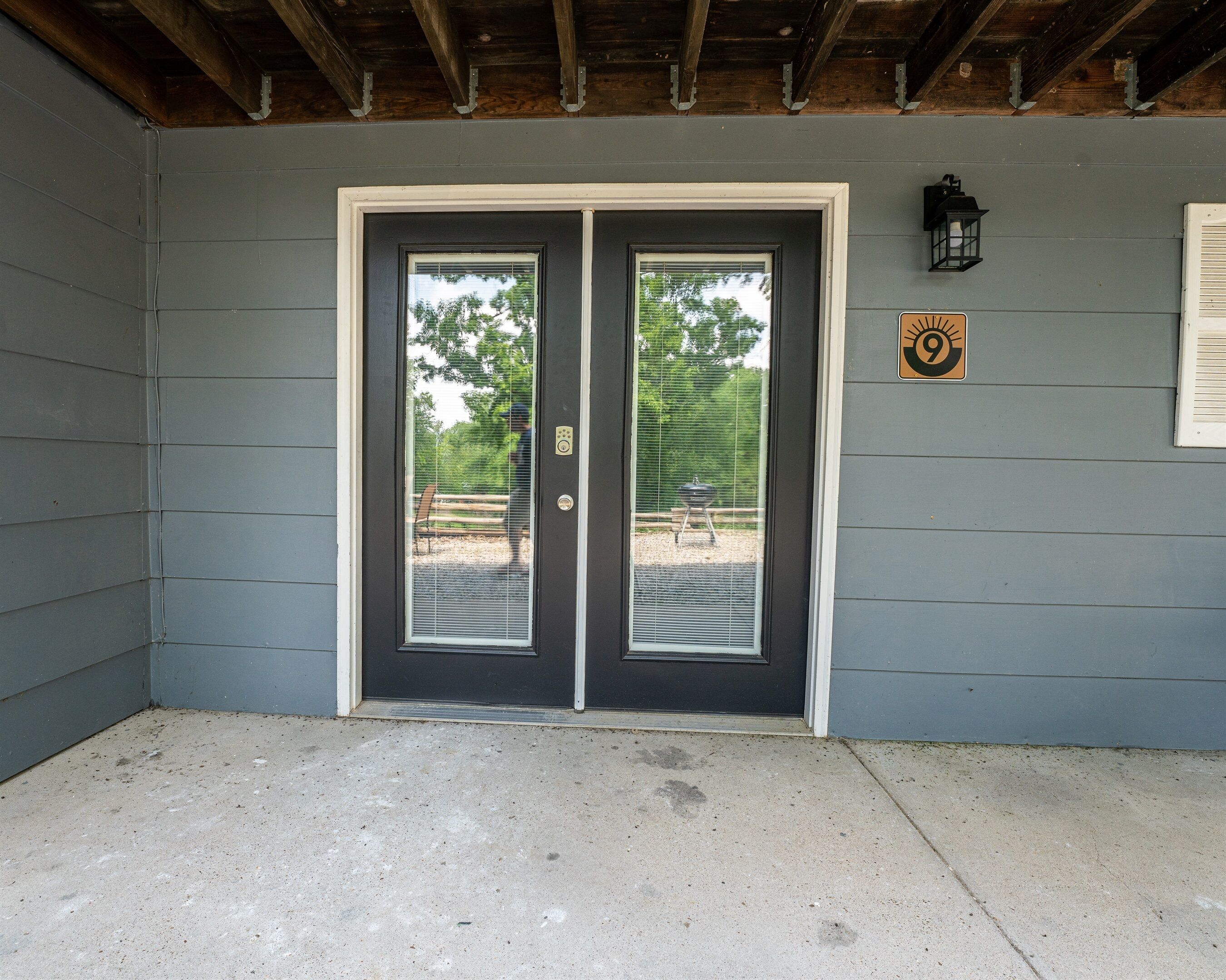 A gray exterior wall with a double door and a small sign with a sun symbol.