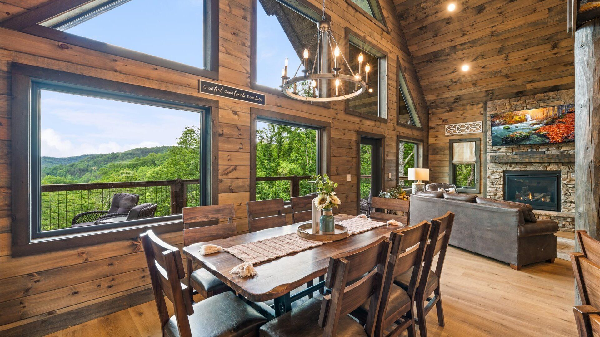 Une cabane en bois comprenant un coin repas, une cheminée et de grandes fenêtres donnant sur une forêt.