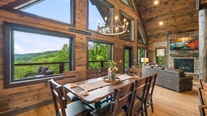 A wooden cabin with a dining area, a fireplace, and large windows overlooking a forest. - Mountain Cabin - Views, Theater, Game Room, Pool (Sevierville)