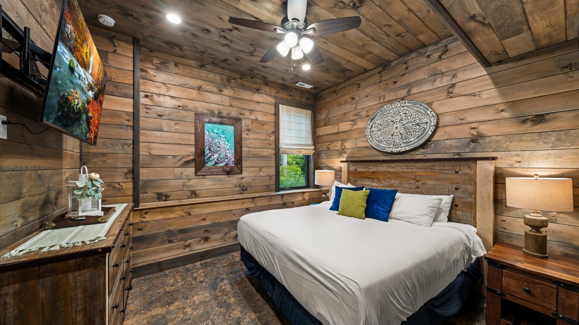 A wooden cabin bedroom with a bed, a nightstand, a ceiling fan, and a wall-mounted TV.