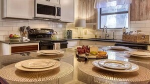 A modern kitchen with white cabinets, a stainless steel microwave, and a large island with woven placemats. - *Romantic 3BD w/ HOT TUB! Nestled in the WOODS!* (Pigeon Forge)