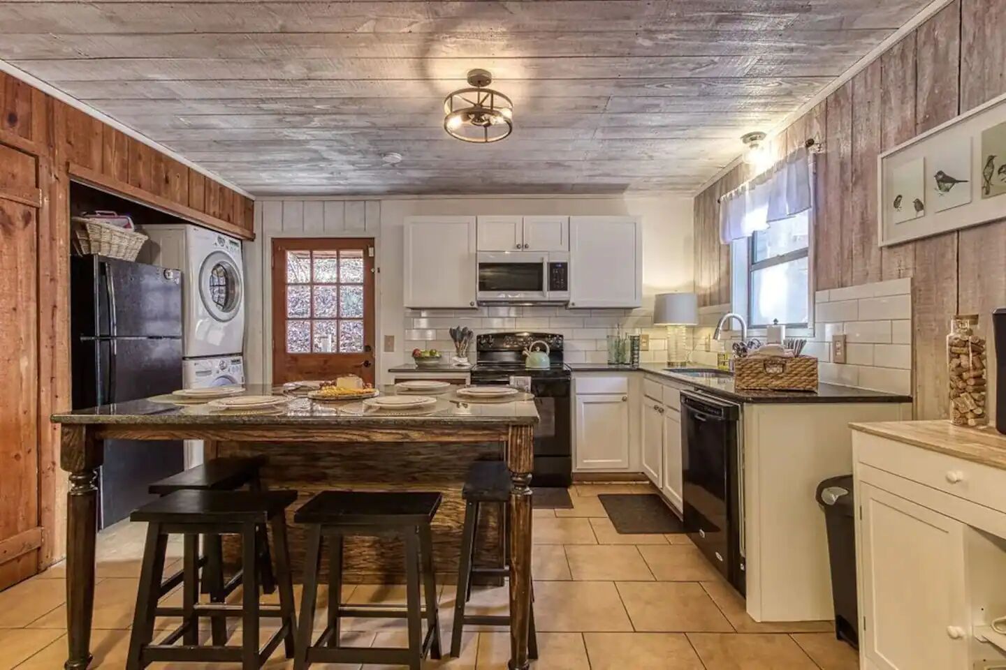 A kitchen with wooden cabinets, a central island with stools, a refrigerator, a microwave, and a sink.