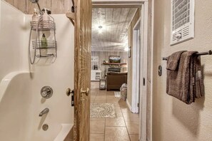 A bathroom with a bathtub, shower, and a wooden door leading to a living area with a fireplace, sofa, and kitchen. - *Romantic 3BD w/ HOT TUB! Nestled in the WOODS!* (Pigeon Forge)