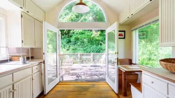 Une cuisine avec des meubles blancs, un plan de travail en bois et une vue sur un jardin, visible à travers une porte ouverte.