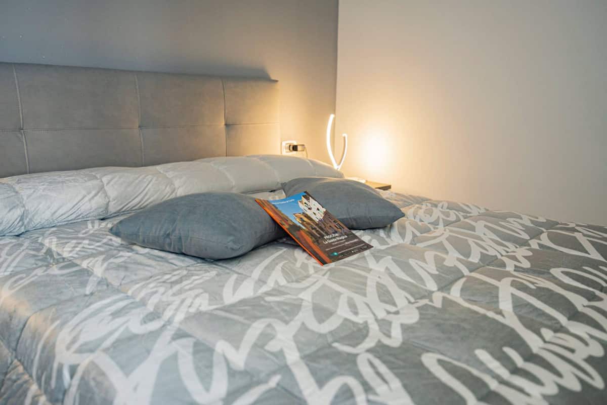 A neatly made bed with a magazine, a headboard, and a wall-mounted light.