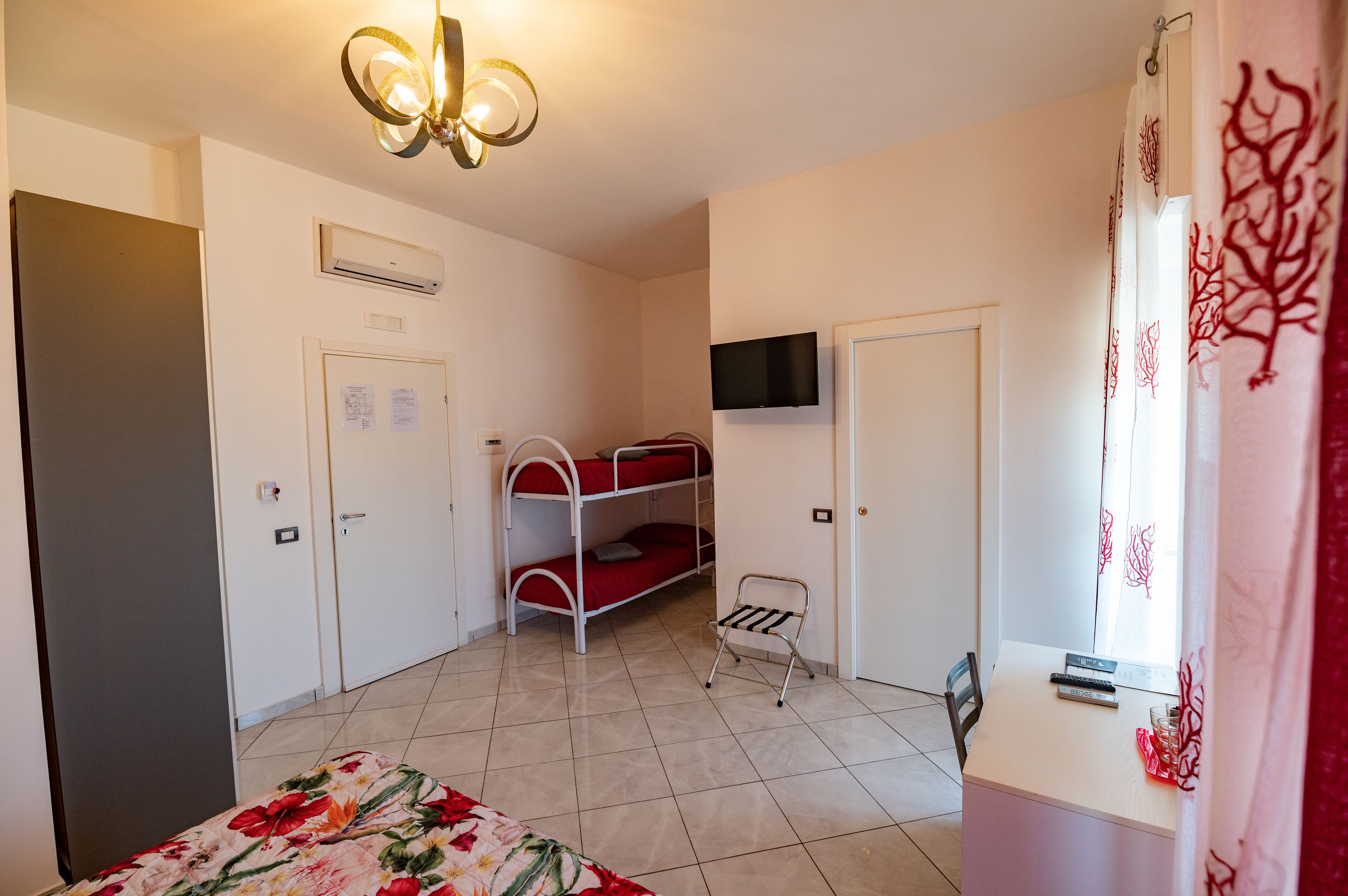 A room with bunk beds, a desk, a chair, a TV mounted on the wall, and an air conditioning unit.
