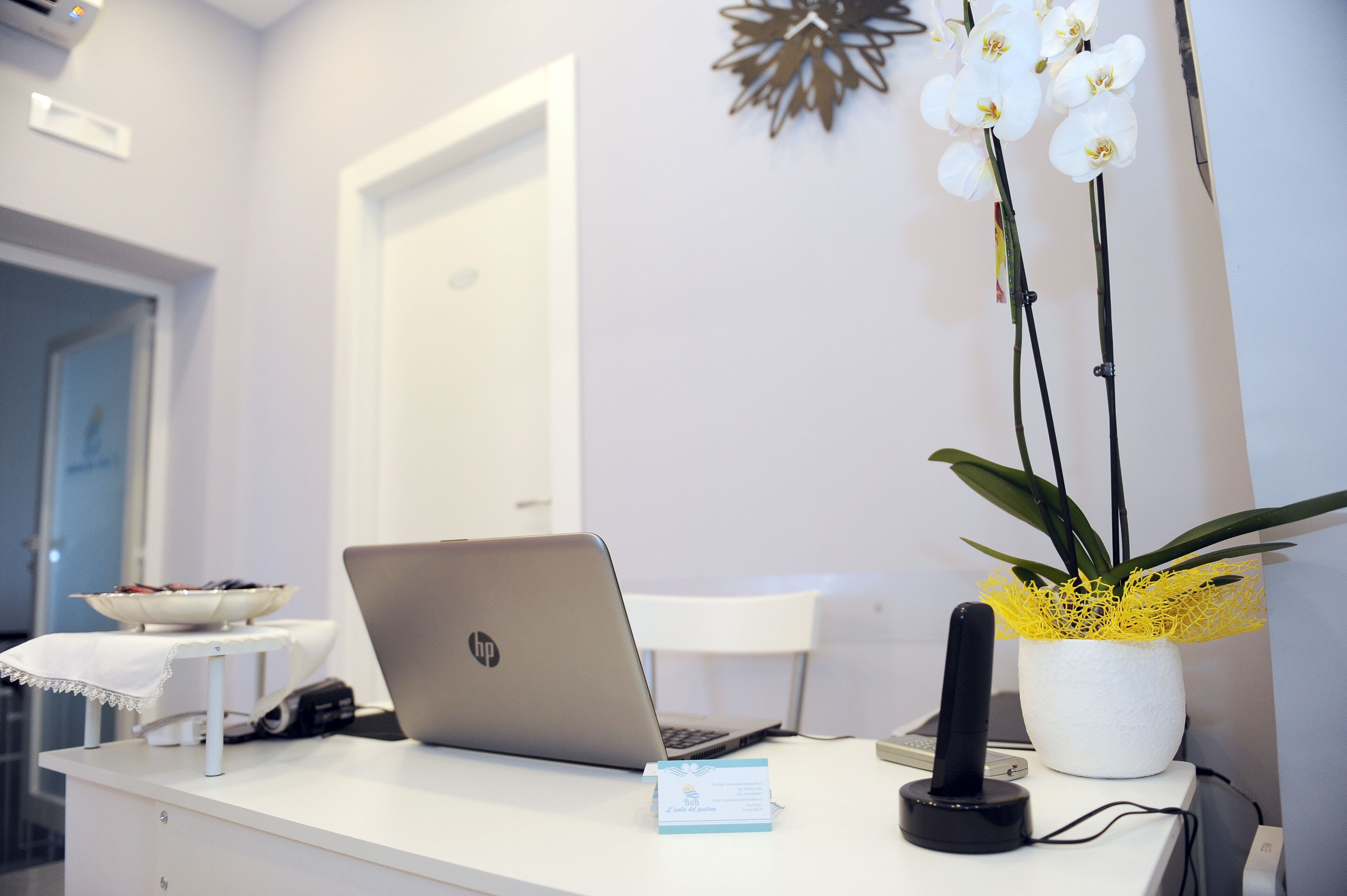 Ein Empfangsschalter mit einem Laptop, einem Telefon, einer Namensschild und einem Blumentopf mit weißen Orchideen.