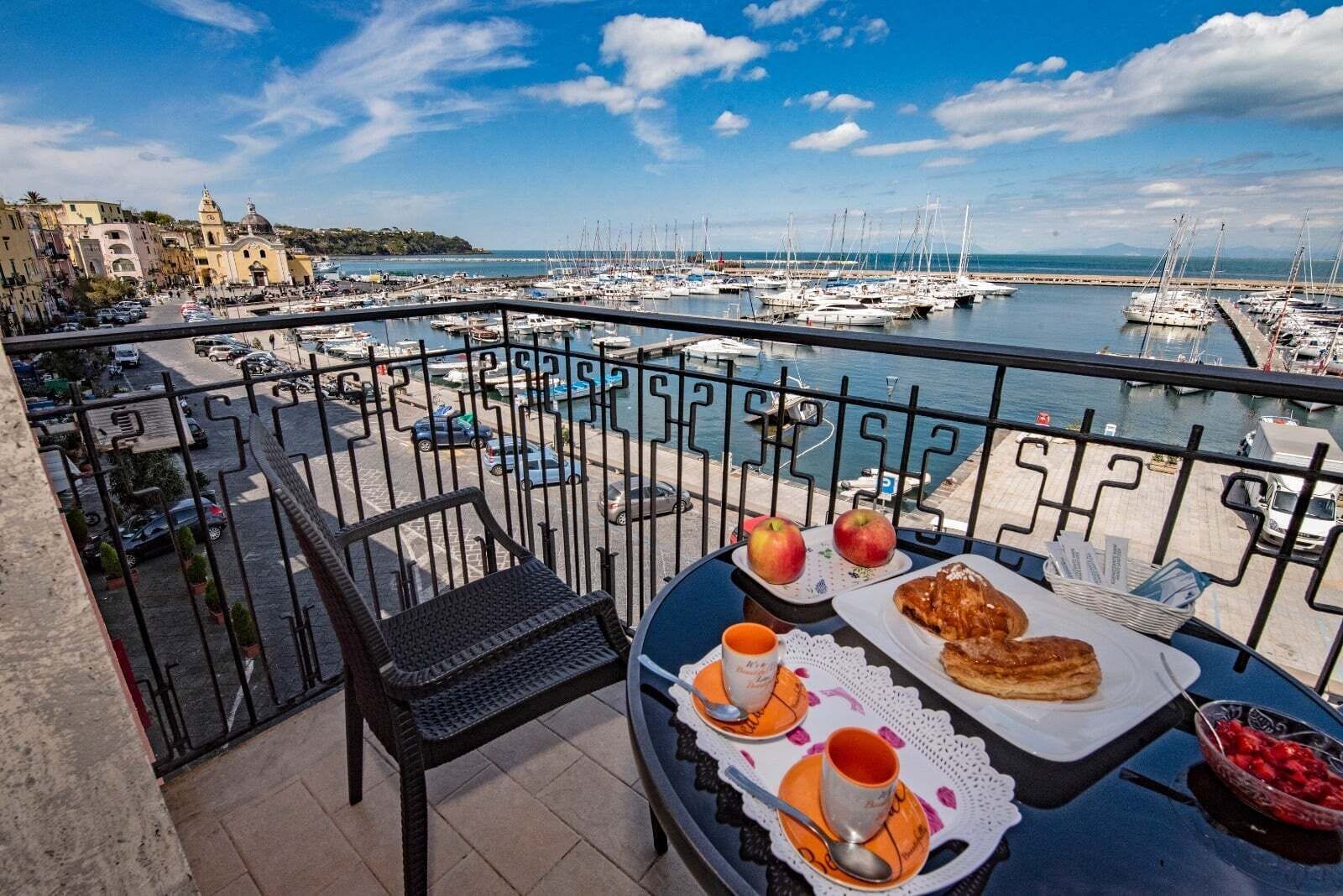 Un balcón con una mesa preparada para el desayuno, con vistas a un puerto deportivo y barcos.