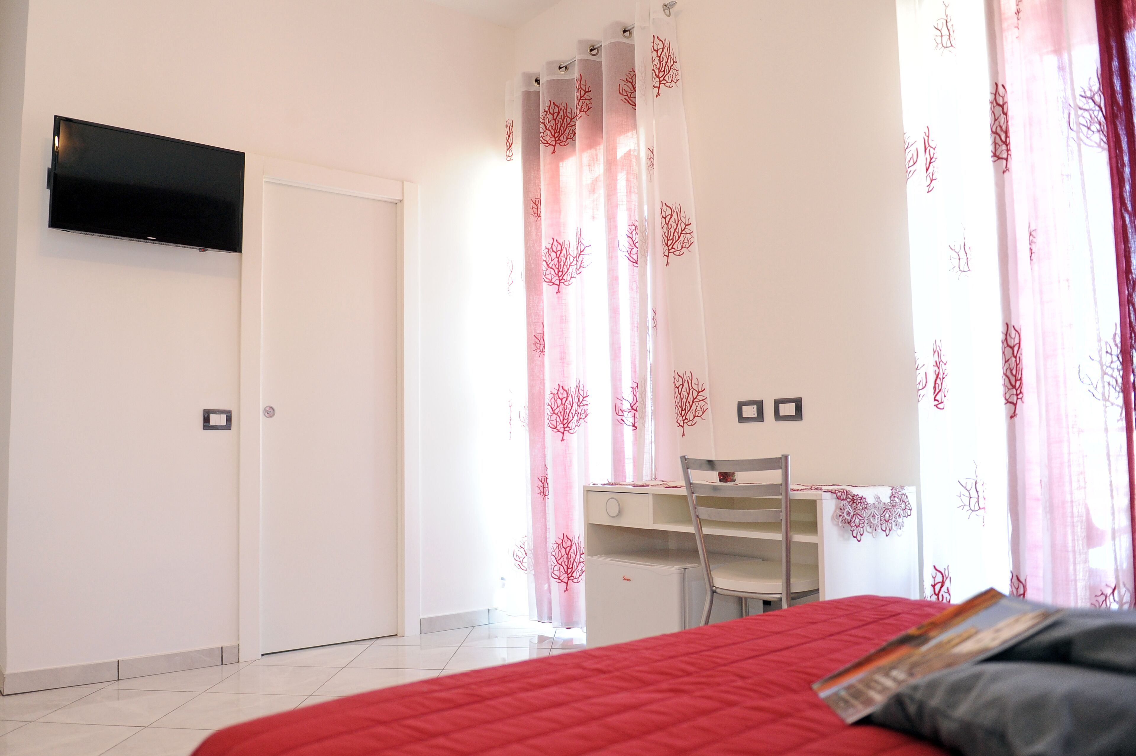 Un dormitorio con cama, escritorio y televisor montado en la pared.
