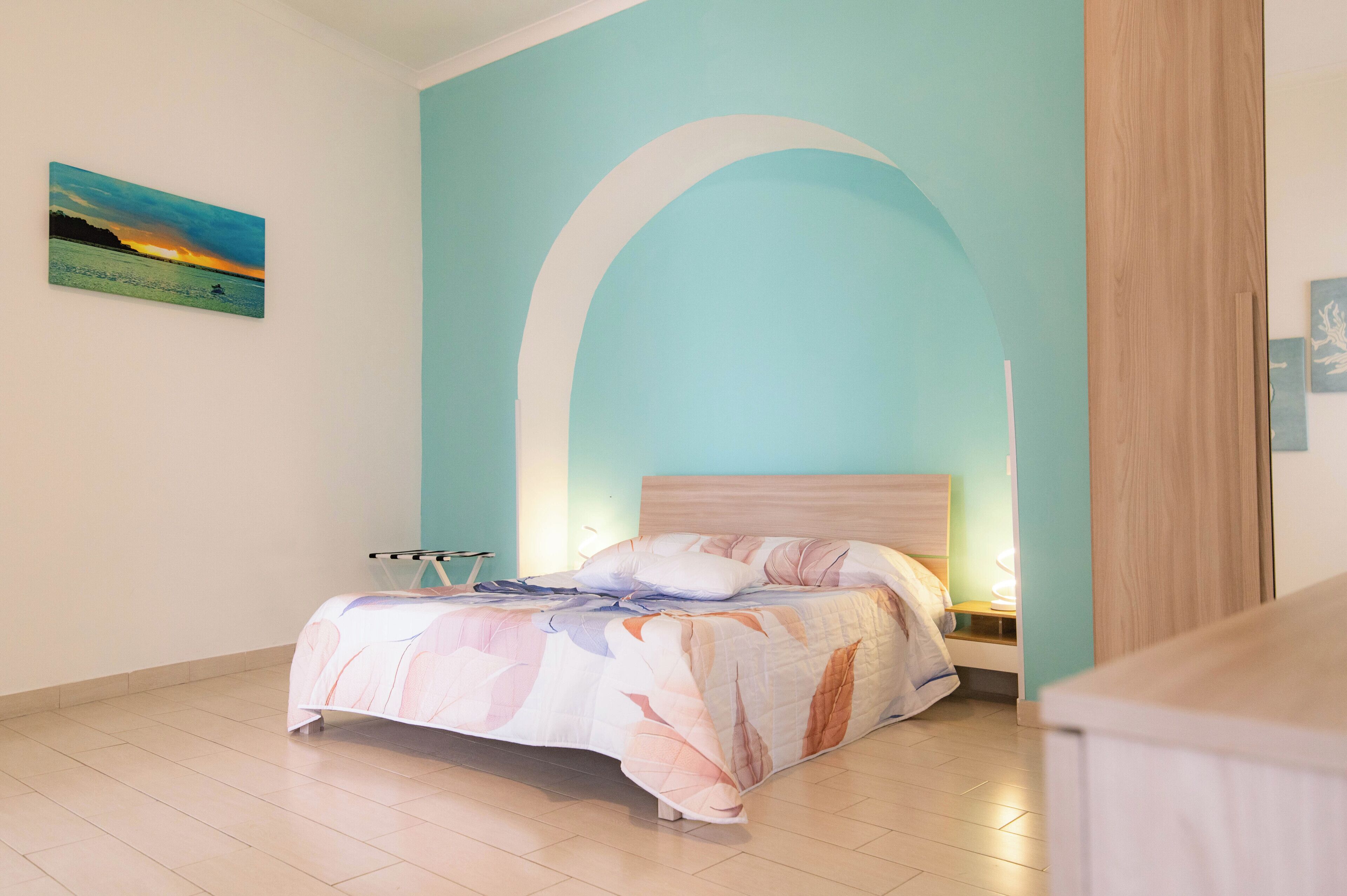 Une chambre à coucher comprenant un lit, une table de chevet, une œuvre d’art accrochée au mur et une porte en bois.