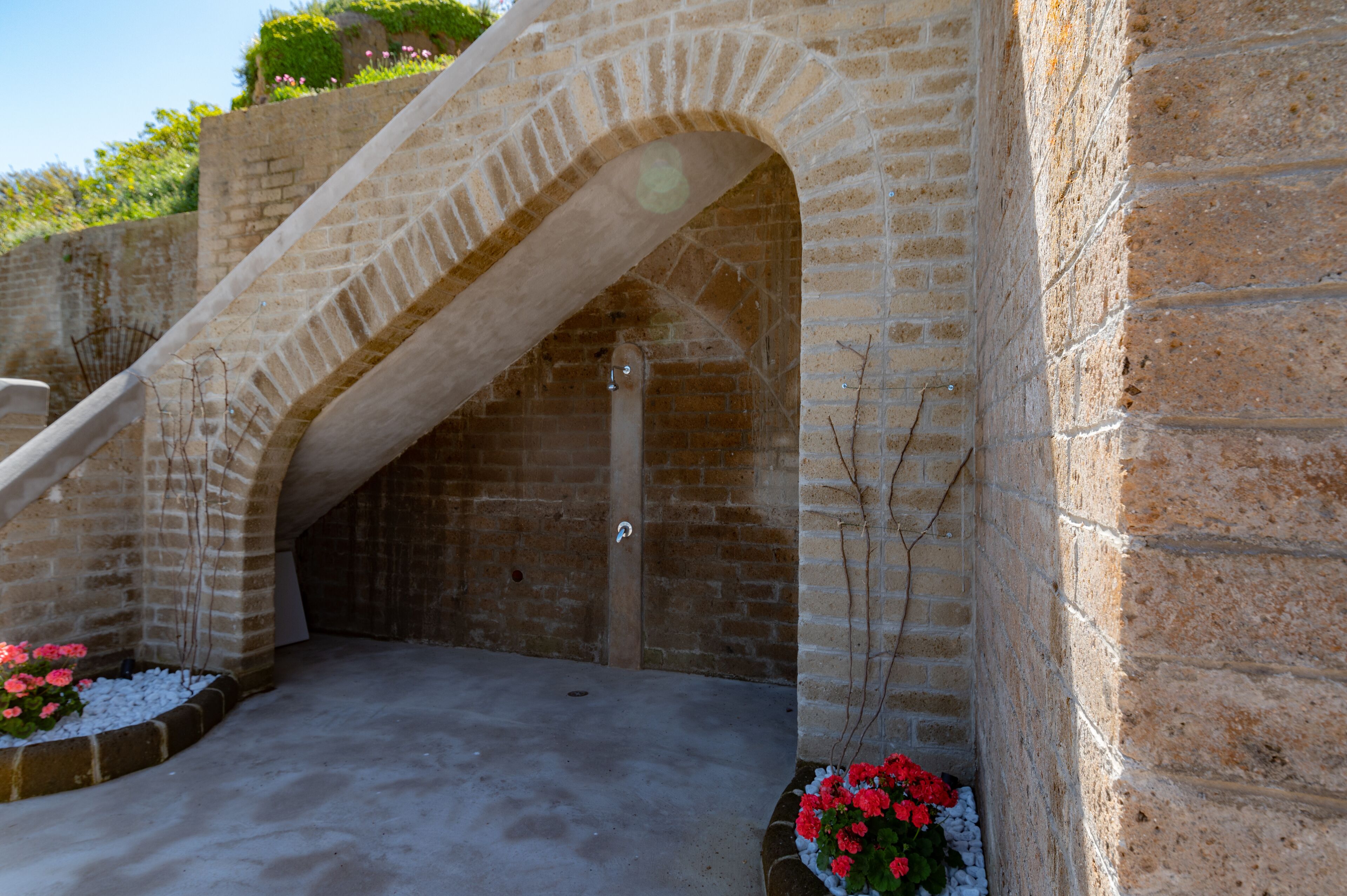 A stone staircase leading to an arched doorway, surrounded by brick walls and potted plants.