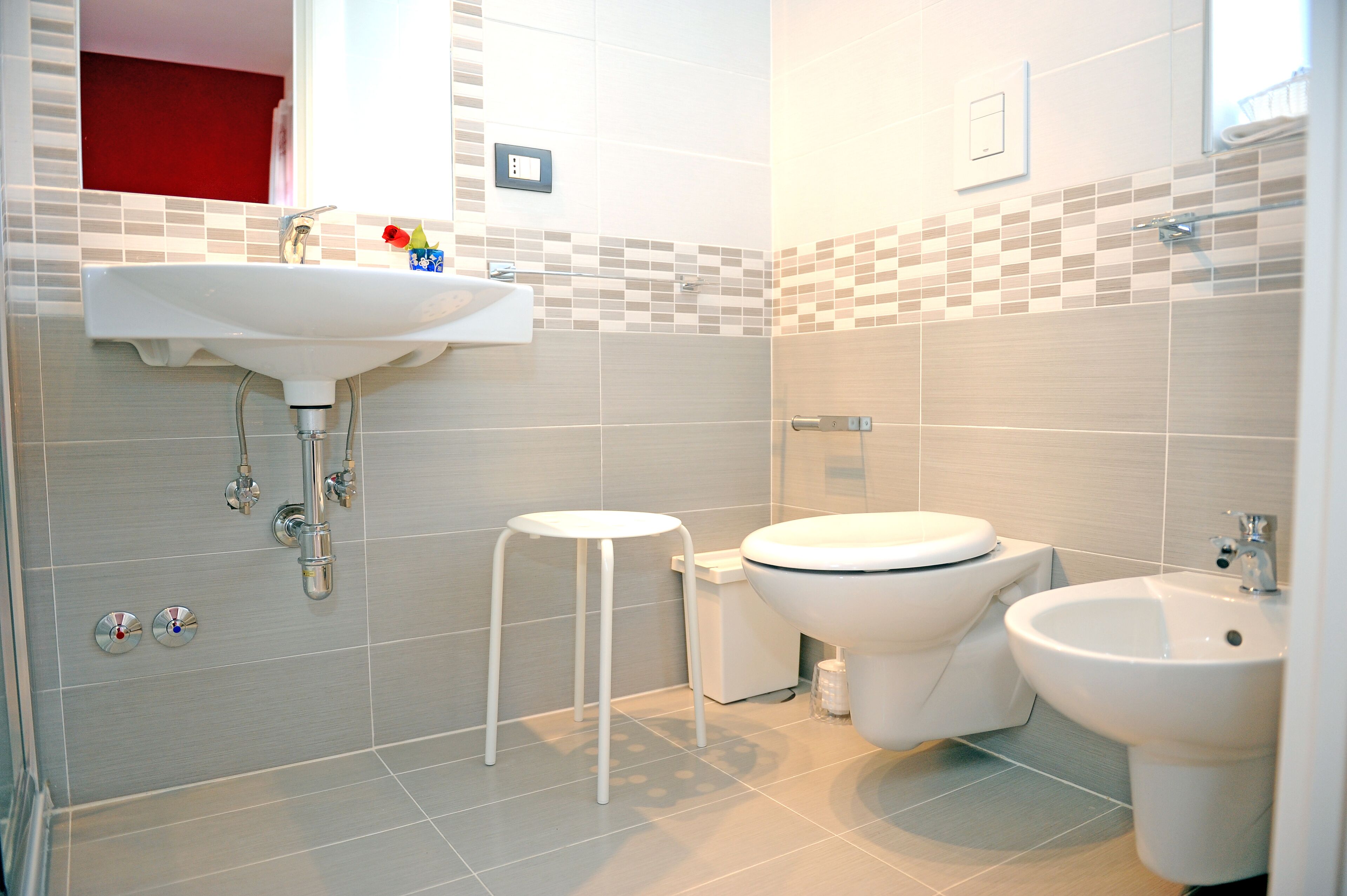 A modern bathroom with a sink, toilet, bidet, and a small white stool.