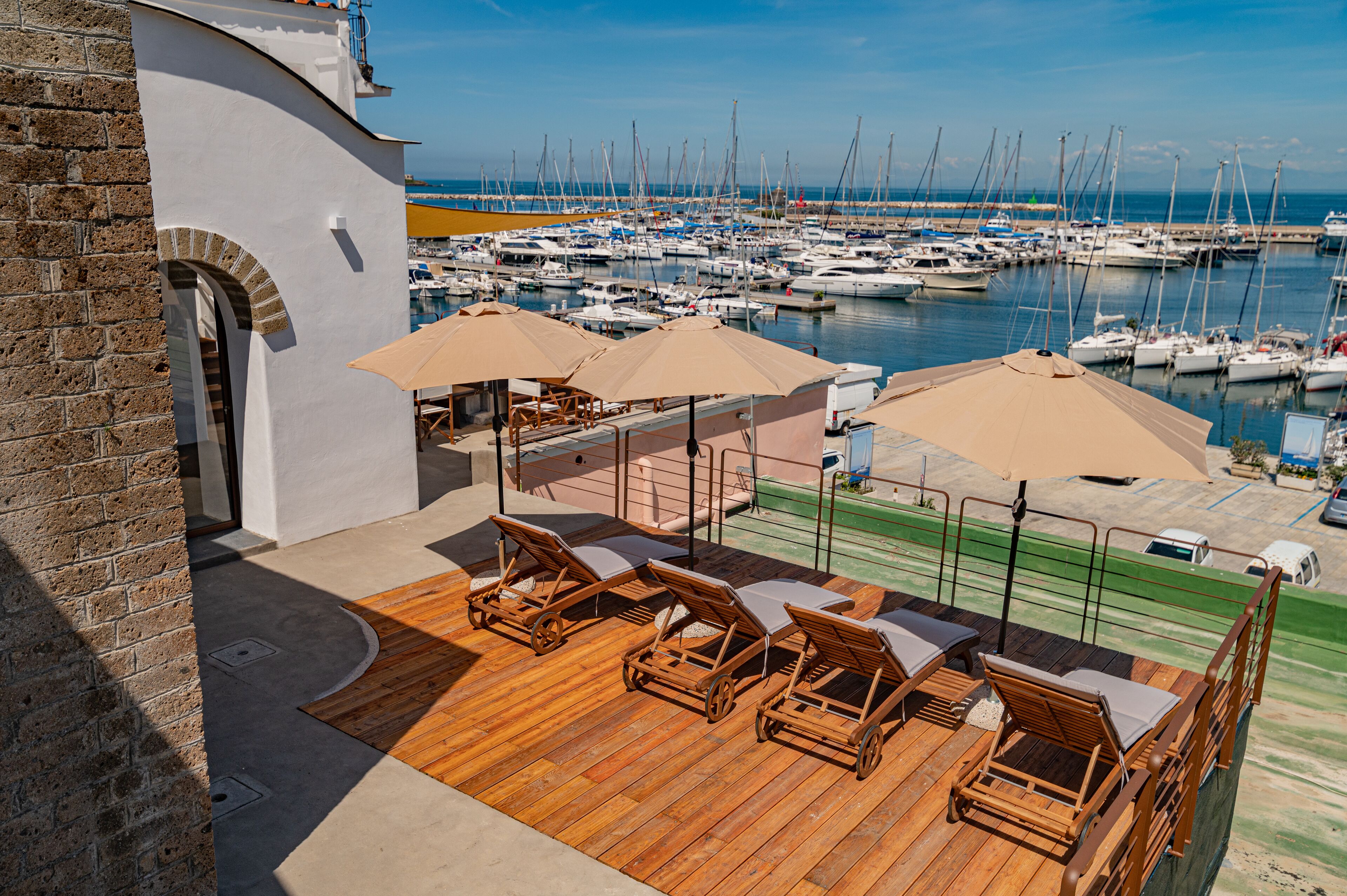 A wooden deck with lounge chairs and umbrellas overlooking a marina with numerous boats.