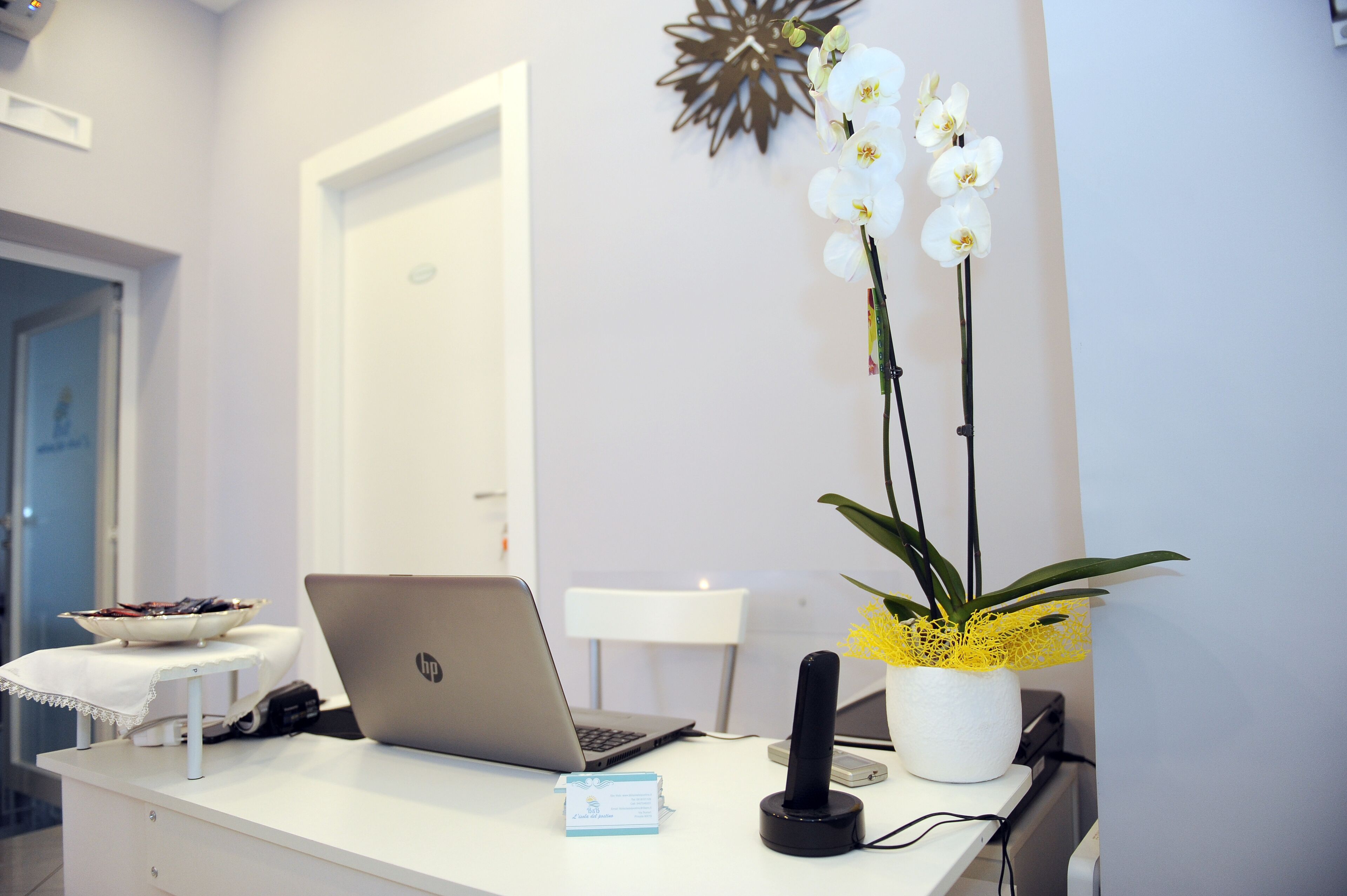 Un escritorio con una computadora portátil, un teléfono y una orquídea en maceta.