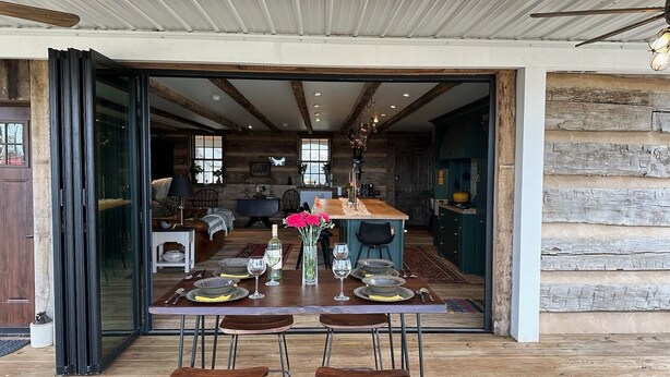 Een open woon- en eetgedeelte met een houten tafel voor vier personen, een bank en een keuken op de achtergrond.