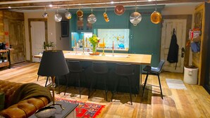 Een moderne keuken met een centraal eiland, zwarte stoelen en hangende pannen.