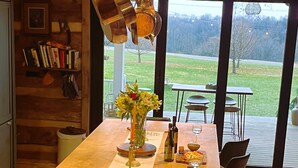 Een keuken met een groot eiland, barstoelen, een eettafel en uitzicht op een gazon door grote ramen.