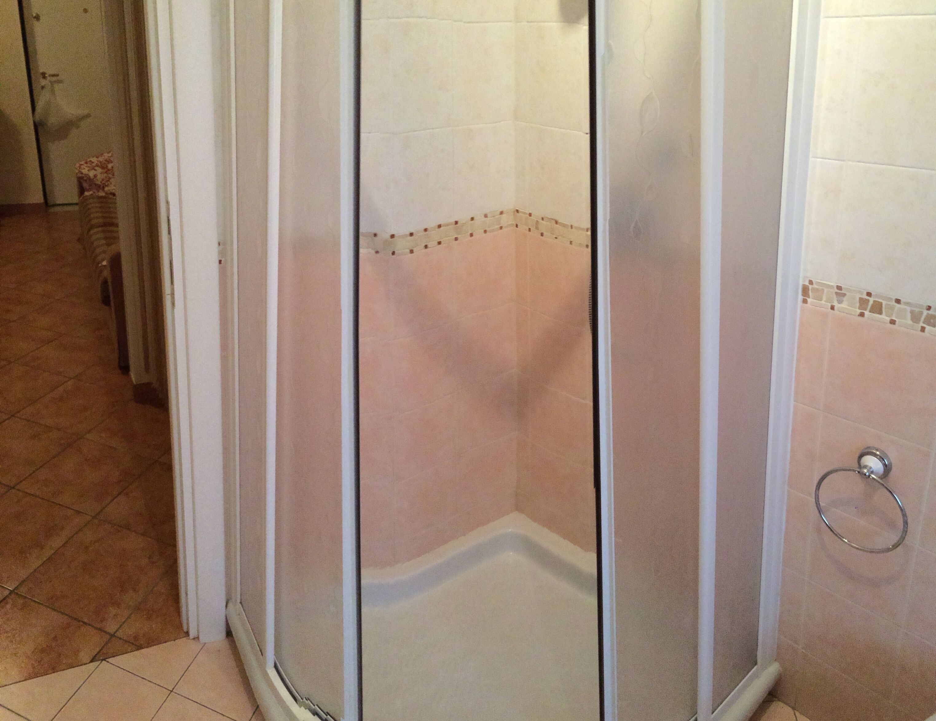 Une douche d’angle avec une porte en verre, des murs carrelés et un sol carrelé.