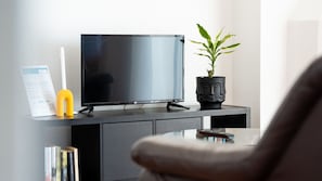 A modern living room with a flat-screen TV on a dark wooden cabinet, a potted plant, and a magazine on a small table.