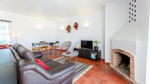 Un salon comprenant un canapé en cuir, une table à manger avec des chaises, un téléviseur, une cheminée et une bibliothèque.