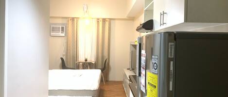 Habitación de hotel con cama, una pequeña mesa con sillas, refrigerador y ventana con cortinas.