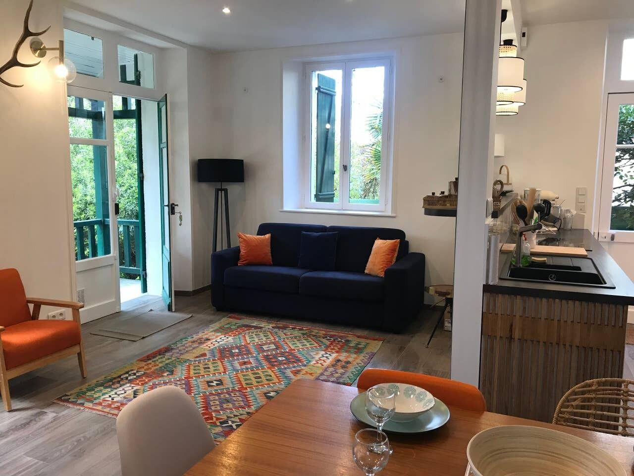 Ein modernes Wohnzimmer mit einer Couch, einem Esstisch mit Stühlen, einem gemusterten Teppich und einer Küchenzeile mit Spüle und Arbeitsplatte.