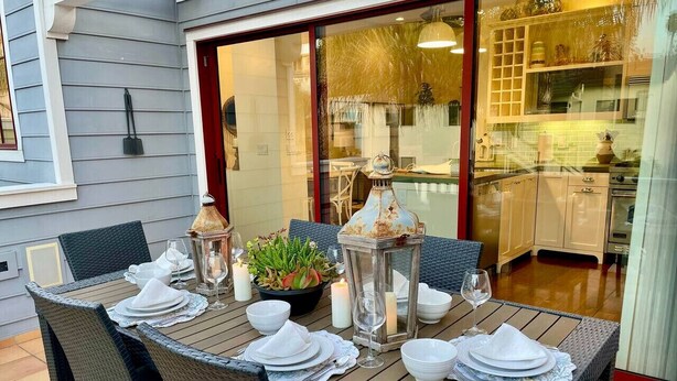 Un área de comedor al aire libre con sillas de mimbre y una mesa de madera dispuesta para una comida, con velas y un centro de mesa.