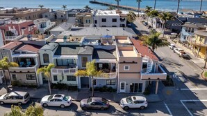 Un área residencial costera con una mezcla de casas individuales y de varios pisos, un muelle que se adentra en el océano y un cielo azul despejado.