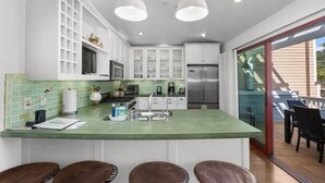 Una cocina moderna con armarios blancos, encimera verde, electrodomésticos de acero inoxidable y una barra con taburetes.