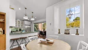 Una cocina moderna con armarios blancos, encimera verde y una mesa de comedor redonda con sillas blancas.