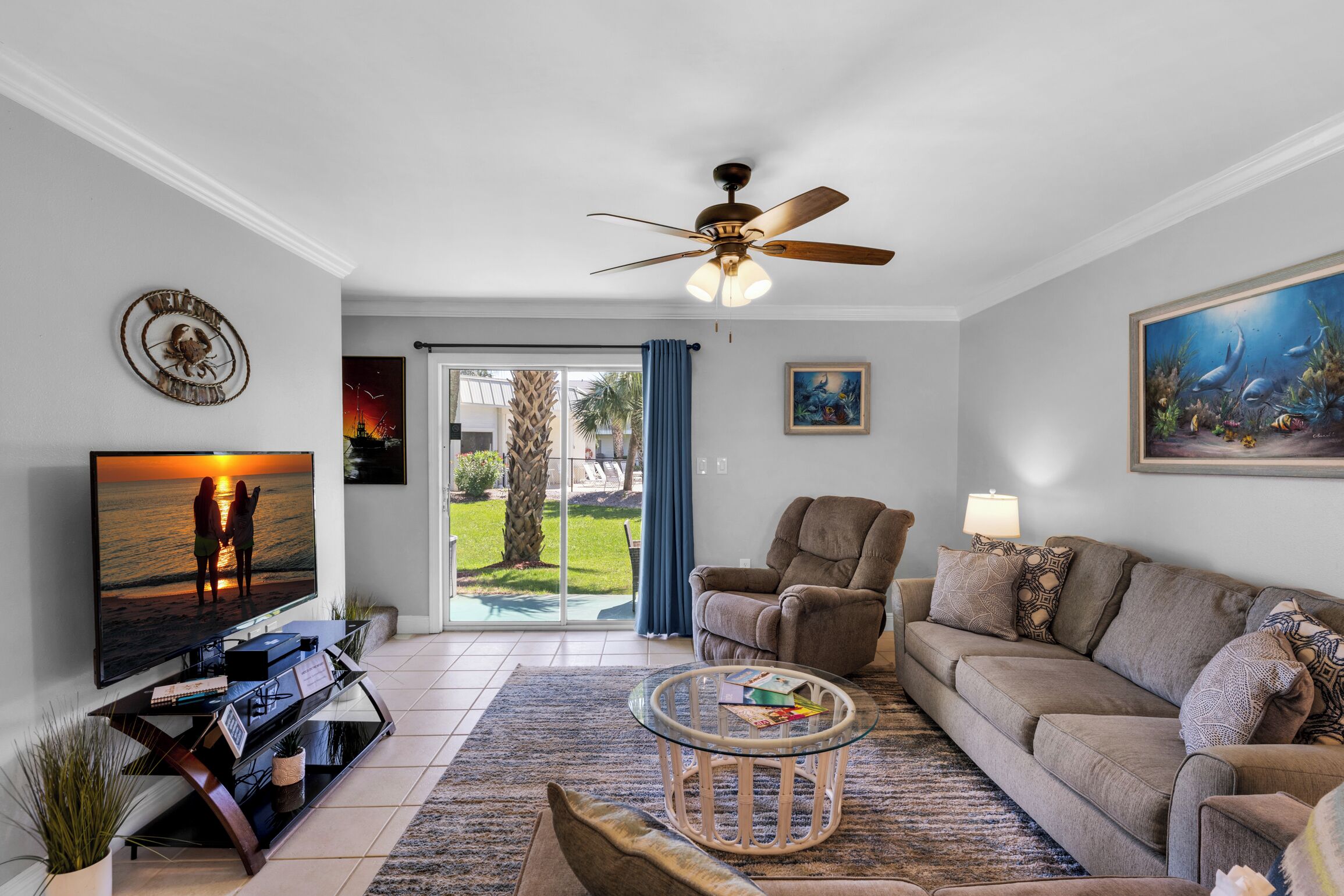 A living room with a flat-screen TV, a ceiling fan, a sofa, a coffee table, and a painting on the wall.