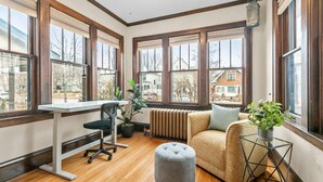 A room with large windows, a wooden floor, a desk with a chair, a sofa, and a small table with a plant. - MINNeSTAY* Lyndale Pleasant Getaway (Minneapolis)