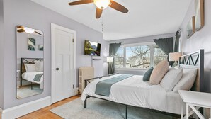 A bedroom with a bed, a ceiling fan, a window with curtains, a radiator, and a TV on the wall. - MINNeSTAY* Lyndale Pleasant Getaway (Minneapolis)