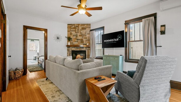 A living room with a sofa, armchair, and a fireplace. There is a ceiling fan, a TV, and a sign that reads 'MINNESOTA'. - MINNeSTAY* Lyndale Pleasant Getaway (Minneapolis)