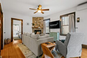 Un salon avec un canapé, un fauteuil et une cheminée. On y trouve également un ventilateur de plafond, un téléviseur et une enseigne sur laquelle on peut lire « MINNESOTA ».