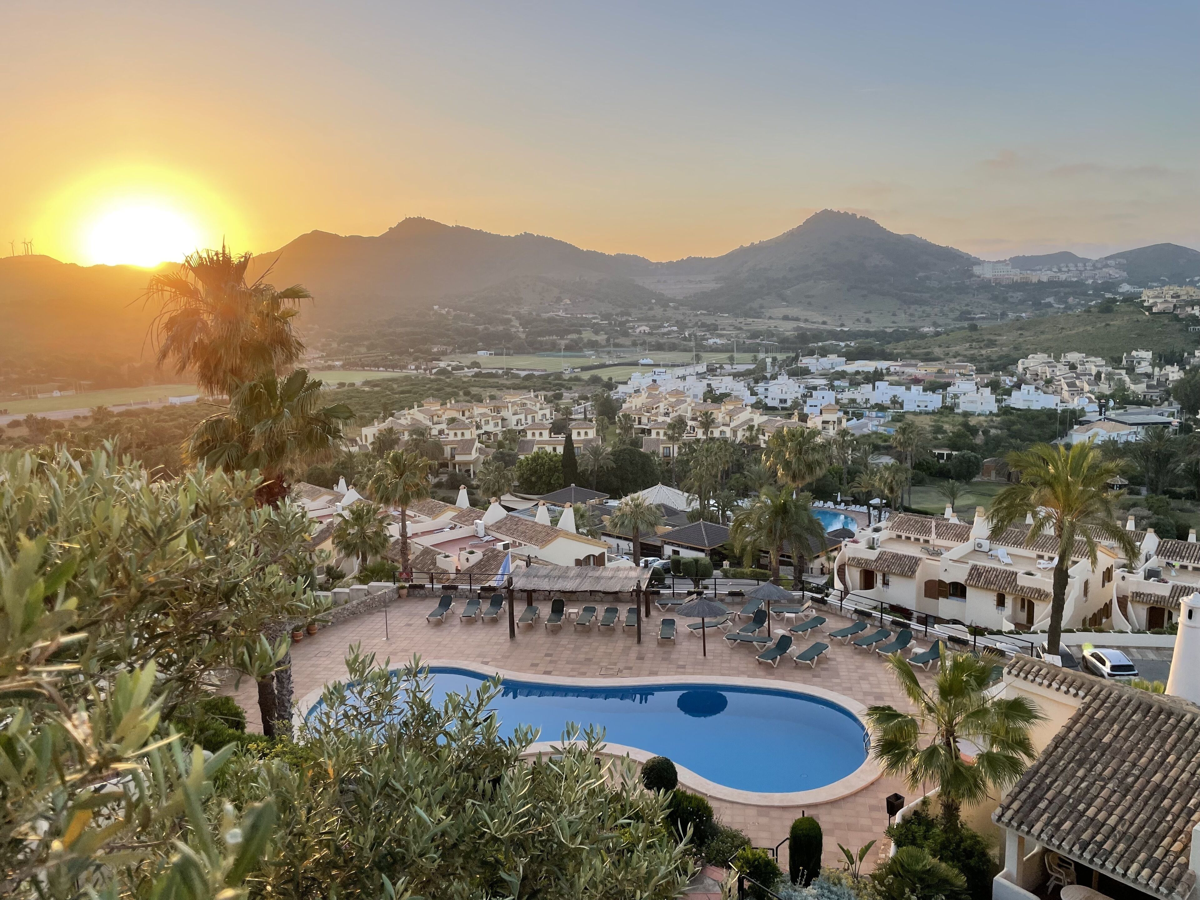 A resort with a swimming pool, lounge chairs, and a view of a town and mountains.