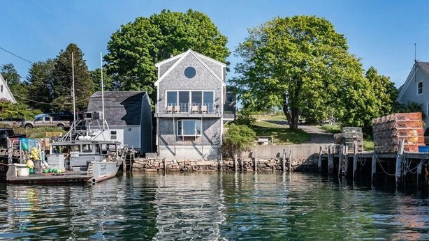 A waterfront property with a house featuring a balcony, docked boats, and a stone pier.